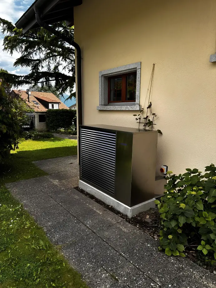 Pompe à chaleur discrète intégrée dans un jardin paysager Pompe à chaleur métallique installée près d’une fenêtre et de plantes dans un jardin