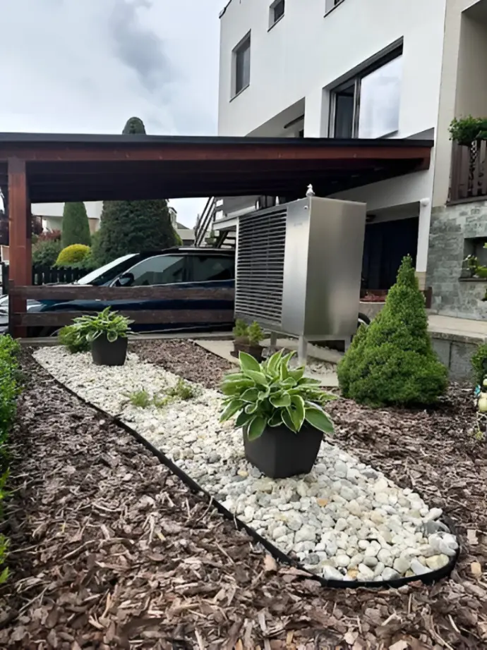 Installation soignée de pompe à chaleur dans un jardin aménagé Pompe à chaleur extérieure installée dans un jardin paysager avec plantes et gravier décoratif