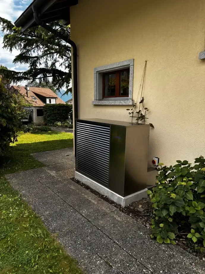 Installation d’une pompe à chaleur résidentielle en Suisse romande Pompe à chaleur résidentielle installée contre un mur de maison en Suisse romande, idéale pour remplacer le chauffage au fioul ou au gaz