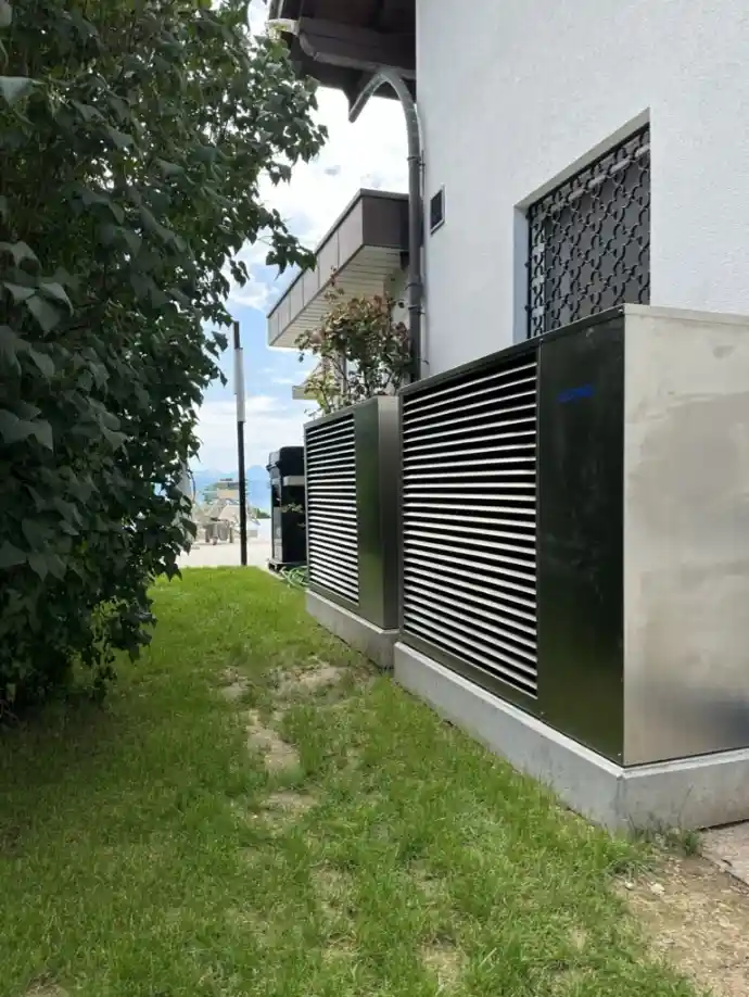 Pompes à chaleur résidentielles installées avec vue sur le lac en Suisse romande Deux unités de pompe à chaleur modernes installées dans un jardin résidentiel en Suisse romande, avec vue partielle sur le lac