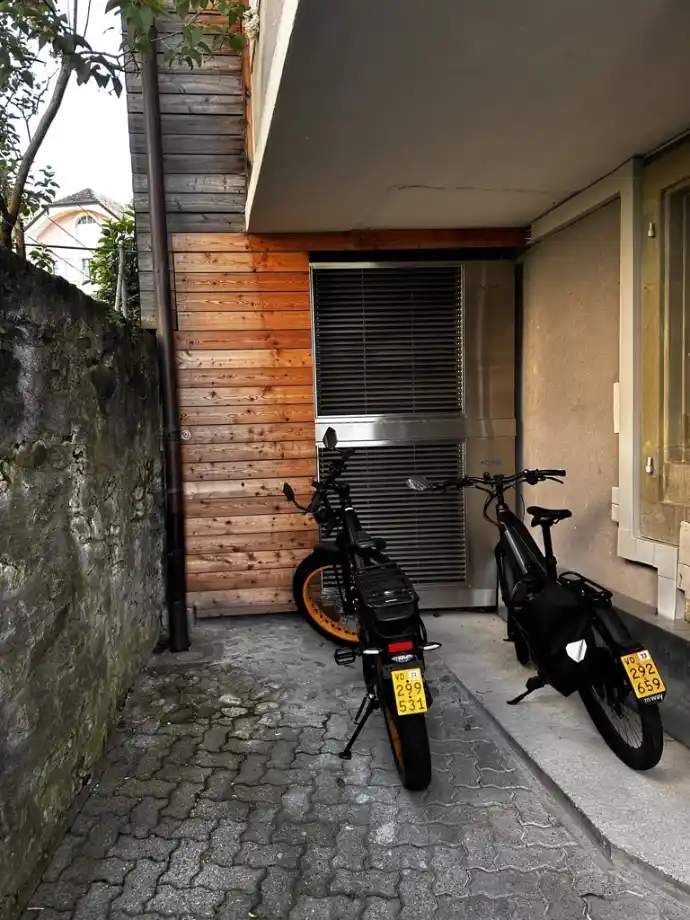Installation discrète d’une pompe à chaleur compacte en Suisse romande Pompe à chaleur compacte installée sous un auvent résidentiel en Suisse romande, à côté de vélos électriques