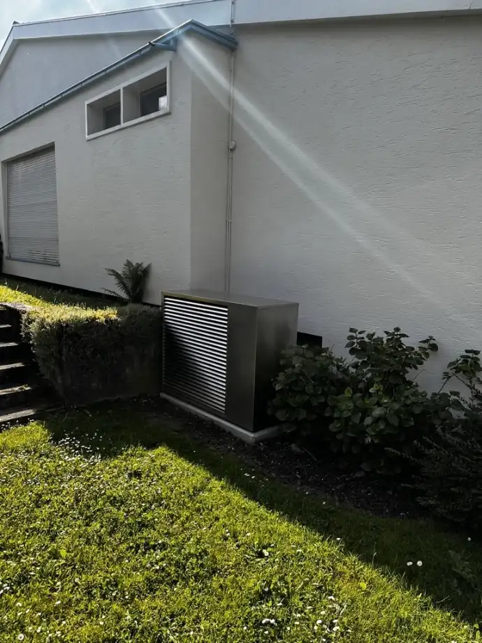 Installation d’une pompe à chaleur résidentielle en Suisse romande Pompe à chaleur résidentielle moderne installée sur le côté d’une maison en Suisse romande avec lumière naturelle